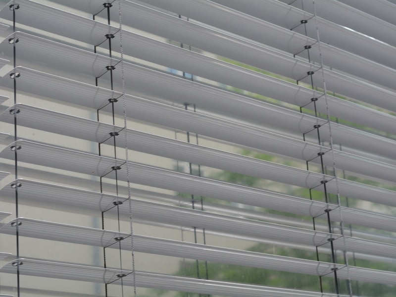 Do Venetian blinds block out light? Close-up of white Venetian blinds partially open, allowing some natural light to pass through.