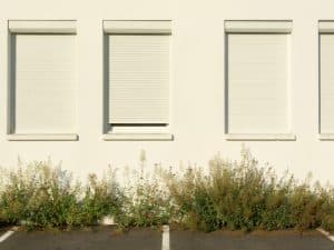 Three white roller shutters on a building facade, one partially open. Do roller shutters reduce noise in urban areas?