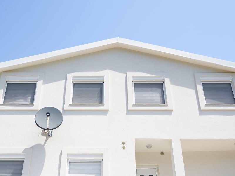 A white house with multiple roller shutters and a satellite dish. Do roller shutters reduce noise from outdoor disturbances?