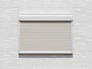 A closed beige roller shutter on a modern brick wall. Do roller shutters reduce noise effectively in homes?