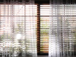 A window with a sheer curtain over blinds, letting soft light into the room.