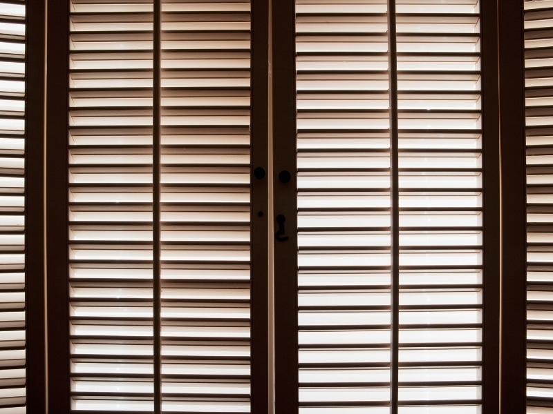 Close-up of timber basswood shutters, highlighting seasonal care for basswood shutters with light filtering through the slats.