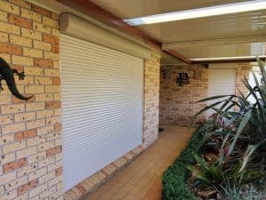 A cream-coloured roller shutter is installed on a brick wall. Considering the building's features, the roller shutter size appears standard for a residential window.