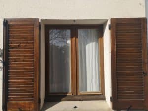 A double window with open timber basswood shutters. For seasonal care for basswood shutters, regular cleaning and oiling is essential.