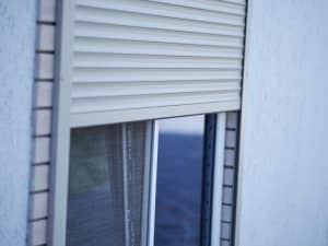 Half-open rolling window shutters fitted over a glass sliding window with flyscreen in a residential home.