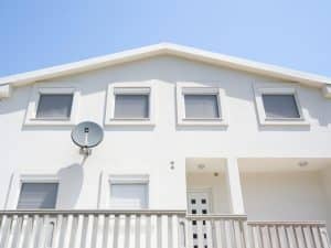 Modern two-storey home with white rolling window shutters covering all visible windows against a clear blue sky.