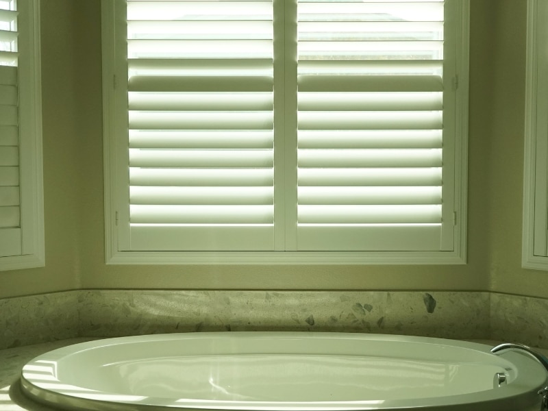 White shutters on bathroom window above a built-in bathtub with natural light