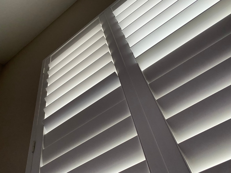 Interior view of white home window shutters filtering natural light