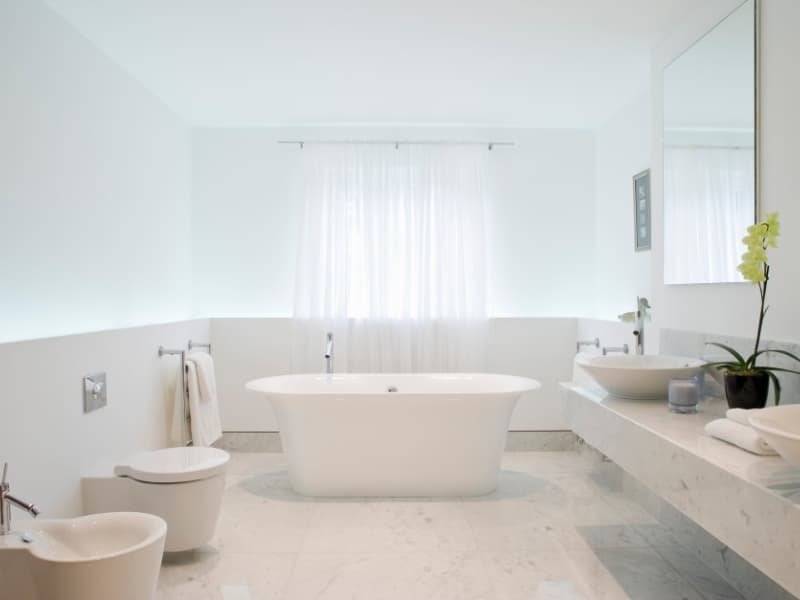 Bright bathroom with freestanding bathtub and sheer curtains instead of shutters on bathroom window