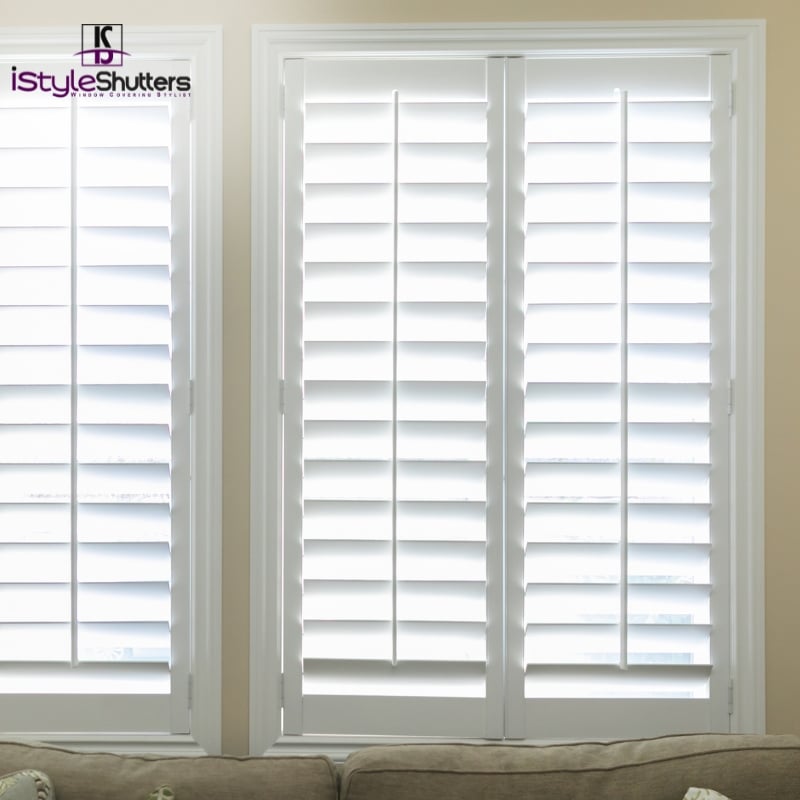 White plantation shutters in Turrella, allowing soft light to filter through, with a beige couch partially visible in the foreground.